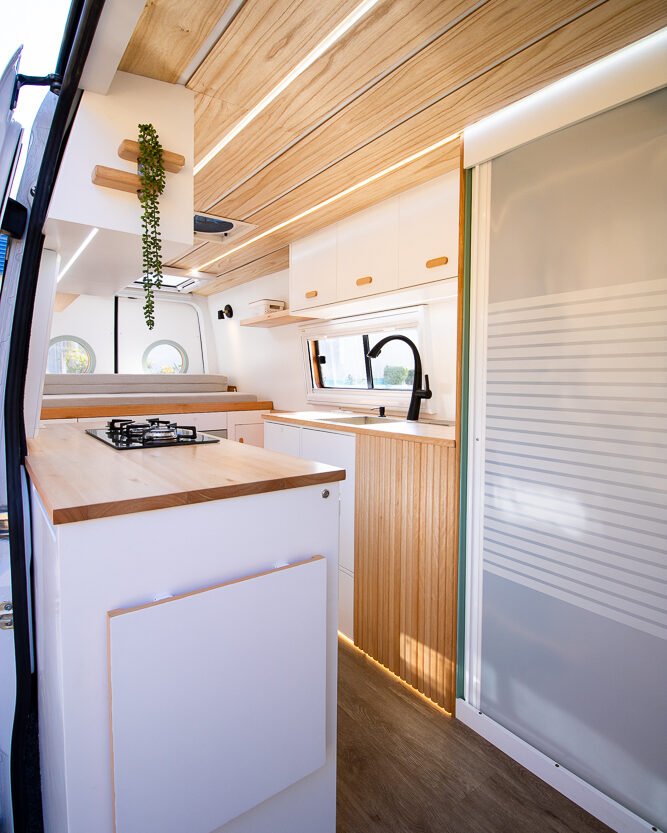 Área de entrada da Sprinter 416 Extra Longa, com mesa retrátil e banco embutido, em tons claros e design moderno